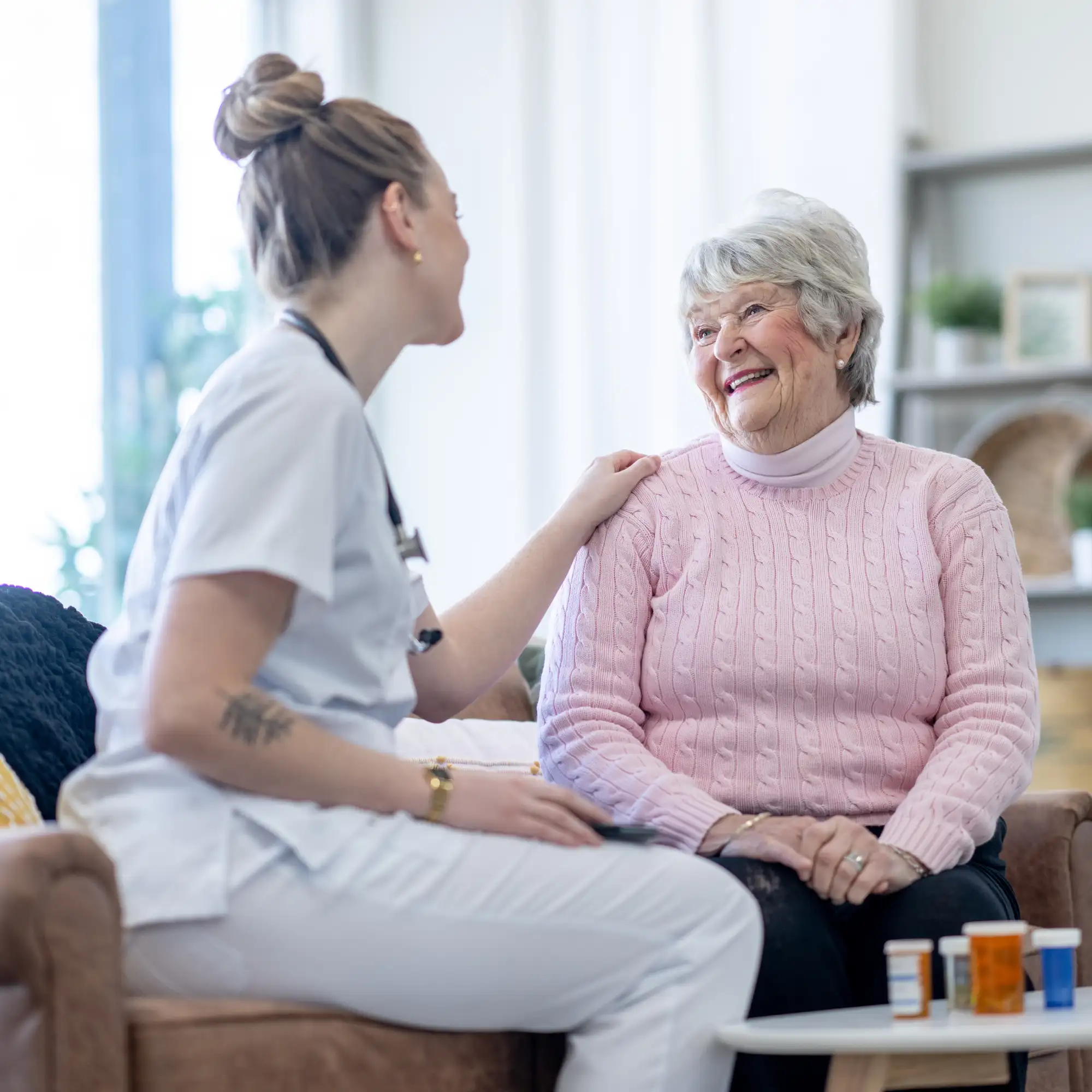 Pflegekraft im Gespräch mit einer Seniorin im Wohnzimmer