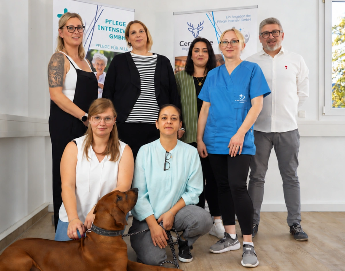 Team der Pflege Intensiv GmbH mit Bürohund vor den Aufstellern von Pflege Intensiv und CervaCare in Werl